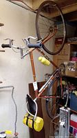 Side view of entire bike hung vertically in basement, showing orange steel frame and 26" wheels.