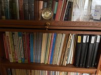Shelf of assorted music books and scores including hardcovers and softcovers arranged in a wooden shelf with a small clock on top