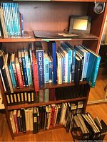 Wooden bookshelf with four shelves containing various car books, magazines, prints sleeves, and a digital picture frame.