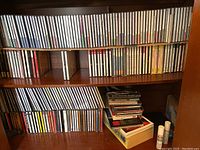 Full bookshelf view showing rows of CDs arranged horizontally and vertically, some stacked with visible titles mainly classical music recordings.