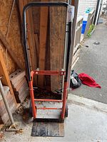 Front view of orange and black 4-in-1 dolly hand truck placed inside a garage near wood planks and bricks.