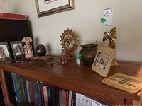 Wide view of the top of a wooden cabinet showing various figurines including a brass dancing figure, black textured sphere, ceramic woman figurine, metal elephant, dark metal pot, and framed prints.