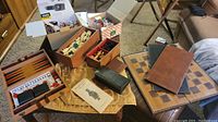 Overview of the lot showing wooden backgammon board, chess pieces in boxes, dominoes, and puzzle games scattered on carpet.