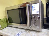 Front view of Breville microwave showing stainless steel finish, door, and digital display with control panel.