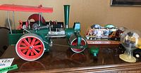Front view of green metal steam tractor with canopy roof and orange plastic rack with cars in background