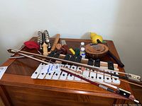 Overview of the lot showing a glockenspiel/xylophone, jingle bells, wooden flute, kalimba, triangle, and violin bows on a wooden surface.