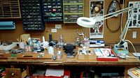 Wide view of wooden workbench with various tools, containers with hardware screws, pens, and small device boxes.