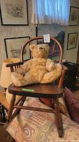 Vintage child's wooden rocking chair with curved back and armrests, holding a plush teddy bear.