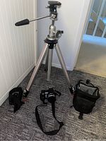 Photo of the Sony DSC-H7 camera, tripod stand, and carrying case arranged together on carpeted floor.