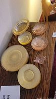 Various pieces of yellow Anchor Hocking Ballerina and pink Jeanette Cherry Blossom pattern glassware arranged on a table including plates and bowls.