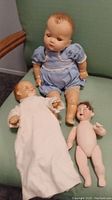 Photo showing all three dolls together including the large baby doll in blue, smaller doll in white gown, and small nude doll.