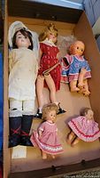 Six vintage dolls in various sizes and conditions placed in a cardboard box, showing overall condition and variety.