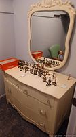 Full view of white dresser with multiple small figurines on top and attached ornate mirror showing its proportion and style.