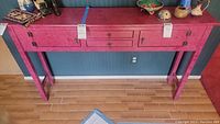Full view of wood entry/console table with reddish surface and metal hardware on cabinet doors and drawers. Various decorative items on top not included.