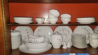 Full set view showing plates, bowls, teacups, teapot, creamer, sugar bowl, salt and pepper shakers arranged on wood shelf.