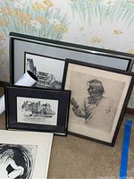Three framed prints and an unframed abstract print leaning against a wall