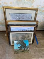 Stack of four framed art prints with various landscape scenes visible behind a bright unframed painting.