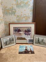 Four paintings shown together, three framed depicting trees and a lake scene, one unframed featuring ships with sails on water.