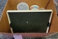 Top view of Lite-Brite board in cardboard box showing white plastic frame and black peg board.