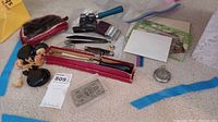 Photo of all items in the lot including razor, cutter, hand warmer, level, pin, stones, and $10 bill case.