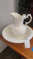 Porcelain white pitcher and basin set shown together with visible design features. Pitcher has chipped top rim.