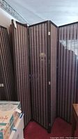 Photo showing two black wood framed folding privacy screens with woven panels, set up in folded form.