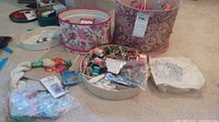 Lot contents showing embroidery thread, pins, needles, cross stitch patterns inside fabric covered containers