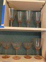 Four taller pink stemware wine glasses with ribbed bowl design on a shelf, bases and stems are pink glass.
