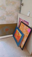 Five abstract art pieces leaning against a wall with floral wallpaper, showing varying sizes and styles.