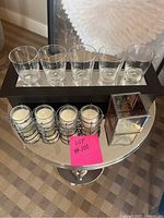 Set of three candle holders on round metallic table. Includes wooden holder with 5 glass votives, metal holder with 4 glass votives, and a square decorative glass holder with dried flowers.