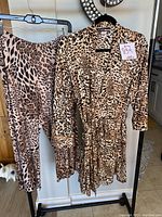 Leopard print robe and pajama bottoms hanging on hangers, showing full front view of both items