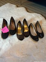 Three pairs of women's shoes on white rug, shoes are brown, black matte, and black patent.