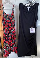 Two sleeveless cotton dresses hanging together on clear plastic hangers: a black scoop neck dress by LEITH showing minimal fading, and a sleeveless floral red and blue dress by Papillon.