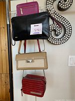 Four women's designer bags and wallets hanging on stand showing Antonio Melani mini bag, red small mini bag, and wallets.