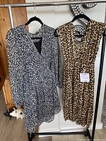Photo showing two women's leopard print dresses hanging on a rack; one black and white, one brown and black