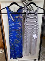 Two sundresses hanging side by side on black hangers; one is blue cotton with a striped pattern, the other is black and white horizontal stripes with a racerback style neckline.