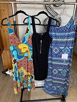 Three women's dresses on hangers shown side by side: colorful Papaya floor-length dress, black zipper front dress, and blue geometric patterned dress.