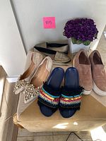 Four pairs of women's shoes arranged on a box, featuring beige slip-ons, pinkish slip-ons, and navy embellished slides