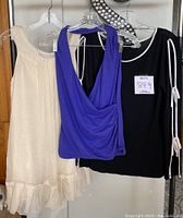 Three women's tops on hangers: cream Cable & Gauge long sleeve top, blue Kenneth Cole Reaction crop halter tank, black Twenty One tank top