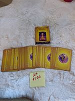 Photo of the full deck of Ascended Masters Oracle Cards fanned out face down with their backs showing, and the guidebook standing upright behind them on a white textured surface.