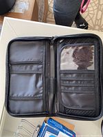 Black nylon travel wallet with multiple zipped compartments and clear card slots, open view