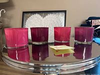 Four glass candle holders placed on a reflective round surface.
