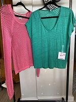 Both sweaters hanging on hangers, green T-shirt and pink crochet sweater visible
