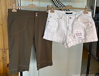 Front view of brown capri pants and white distressed denim shorts hanging on hangers