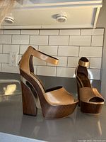 Tan leather platform heels with wooden block heels and ankle strap, shown from side view on a counter against white tile backsplash.