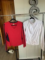 Two women's athletic tops hanging side by side on a rack, one white full zip Zella jacket and one red long sleeve top with black details