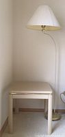 Small cream-colored side table with brass strip edge next to brass and white floor lamp