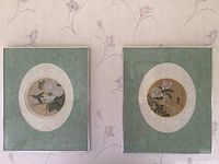 Two framed Asian art prints on wall, floral and fauna themes, green oval matting.