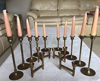 Front view of two sets of brass candle holders with pink taper candles inserted, showing graduated sizes.