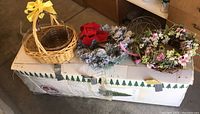 Photo of two wicker baskets, one with a yellow bow, two decorative wreaths placed on top of the box containing the artificial Christmas tree.